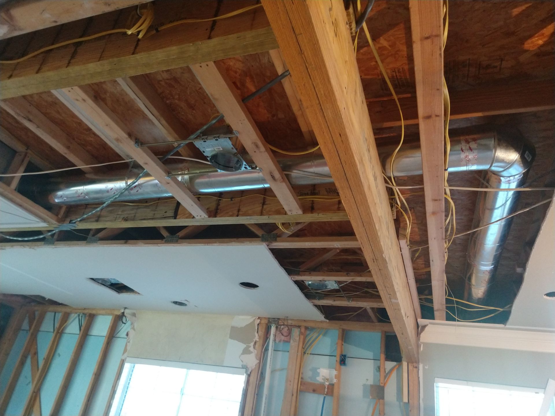 Exposed basement ceiling with wooden joists, ductwork, wiring, and hanging drywall during renovation