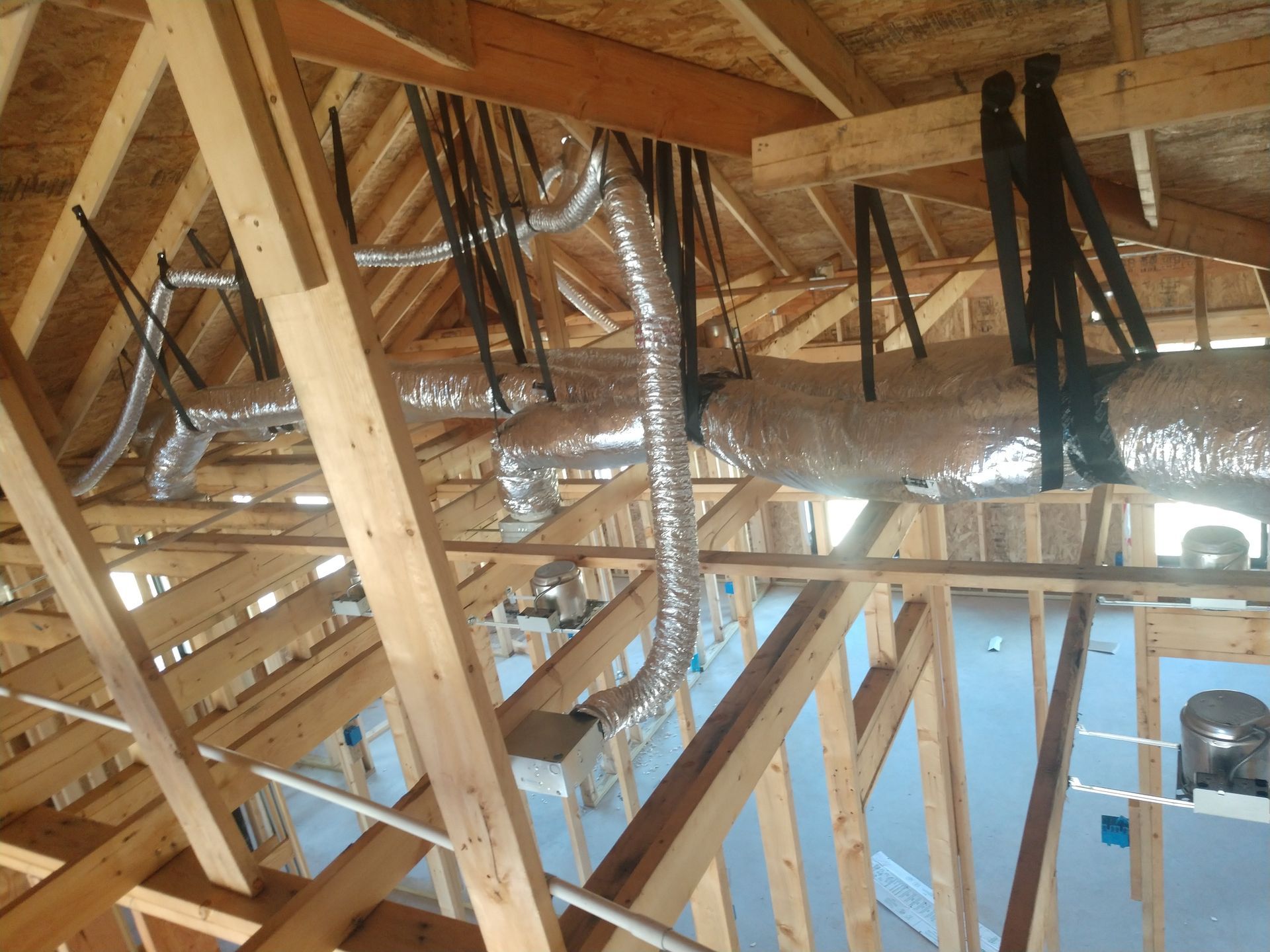 Exposed attic framing with wooden beams, ductwork, and insulation under a sloped roof.