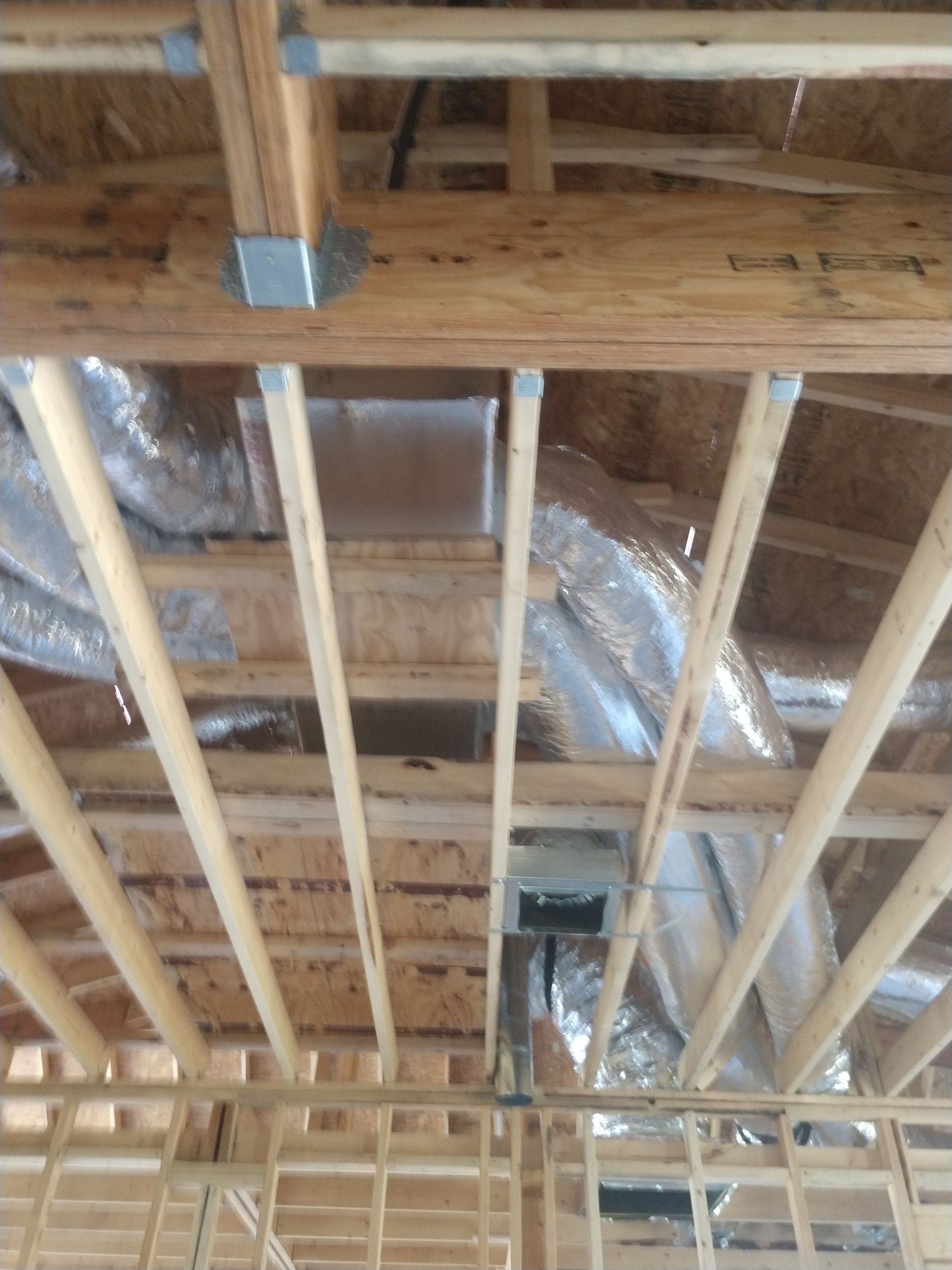 Exposed wooden ceiling joists and HVAC ducts in an unfinished building interior.