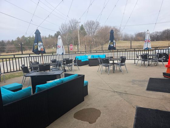 Outdoor patio with turquoise couches, tables, closed umbrellas, and a railing overlooking a wet landscape.