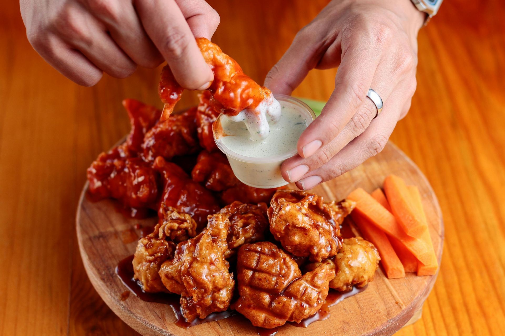 A person is dipping a chicken wing in ranch dressing.