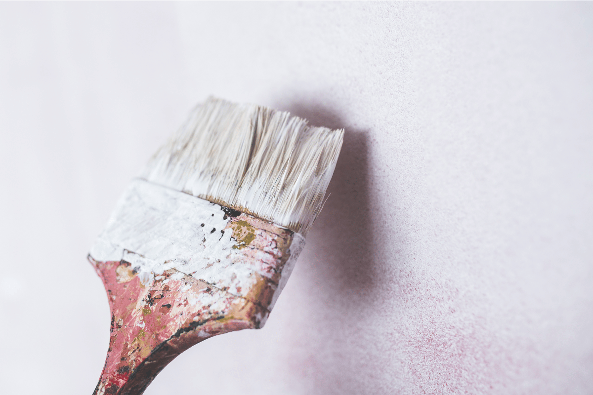 Paintbrush with white paint on a pale wall, leaving a soft pink smudge