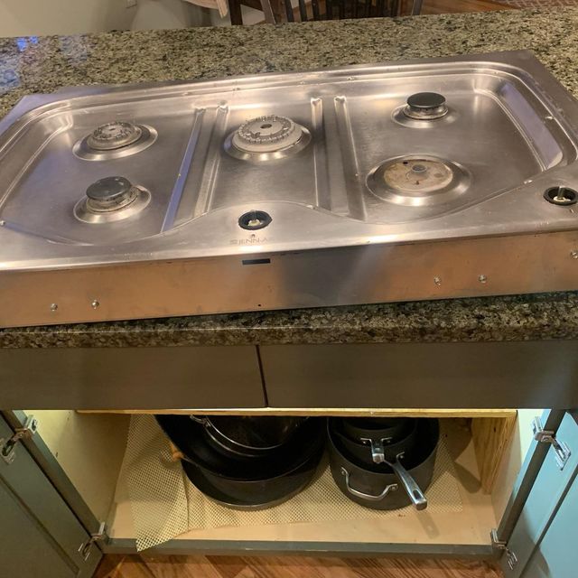 Kitchen sink with open cabinet doors, exposing plumbing and disposal under a granite countertop.