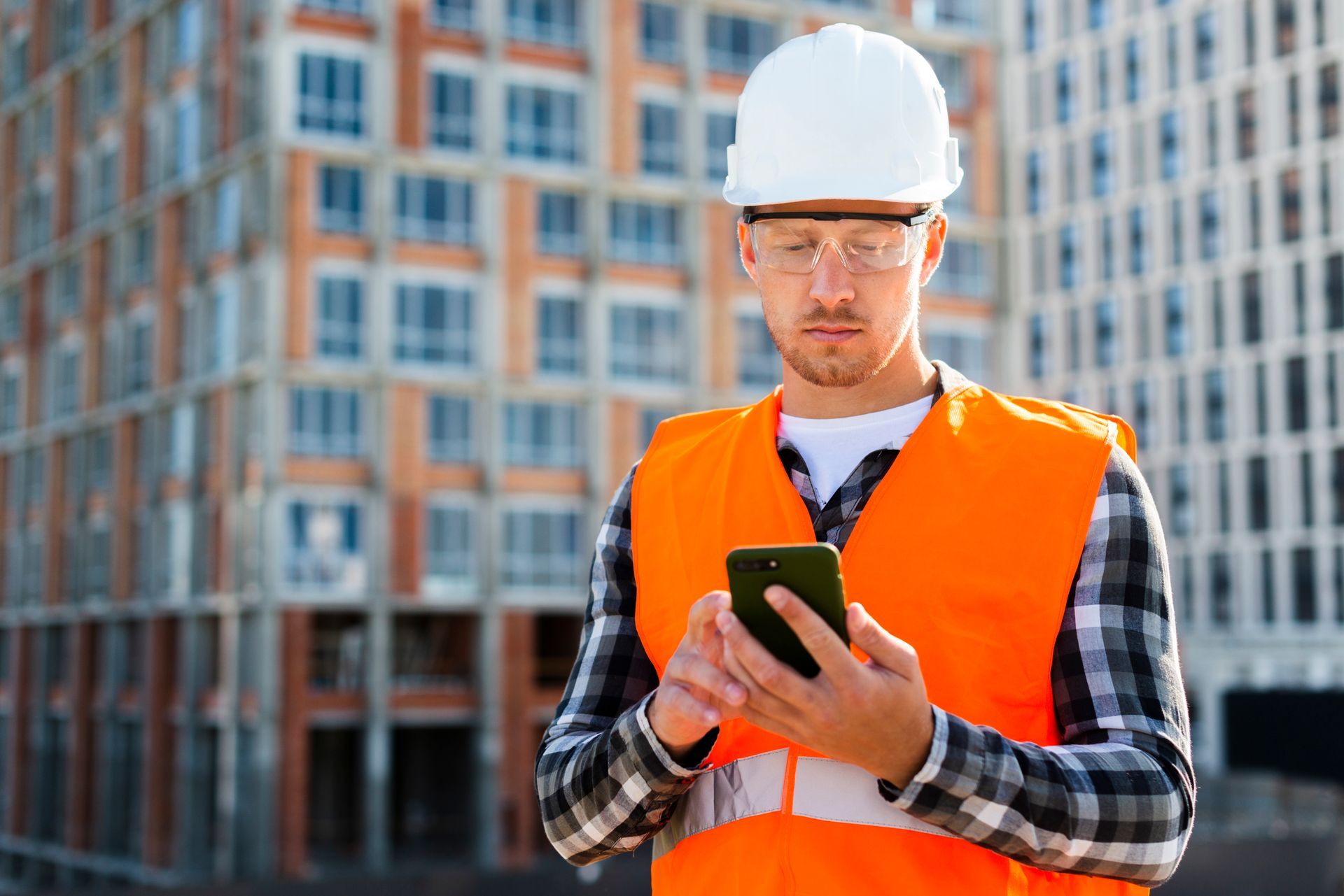 homem com uniforme industrial usando o celular em um canteiro de obras