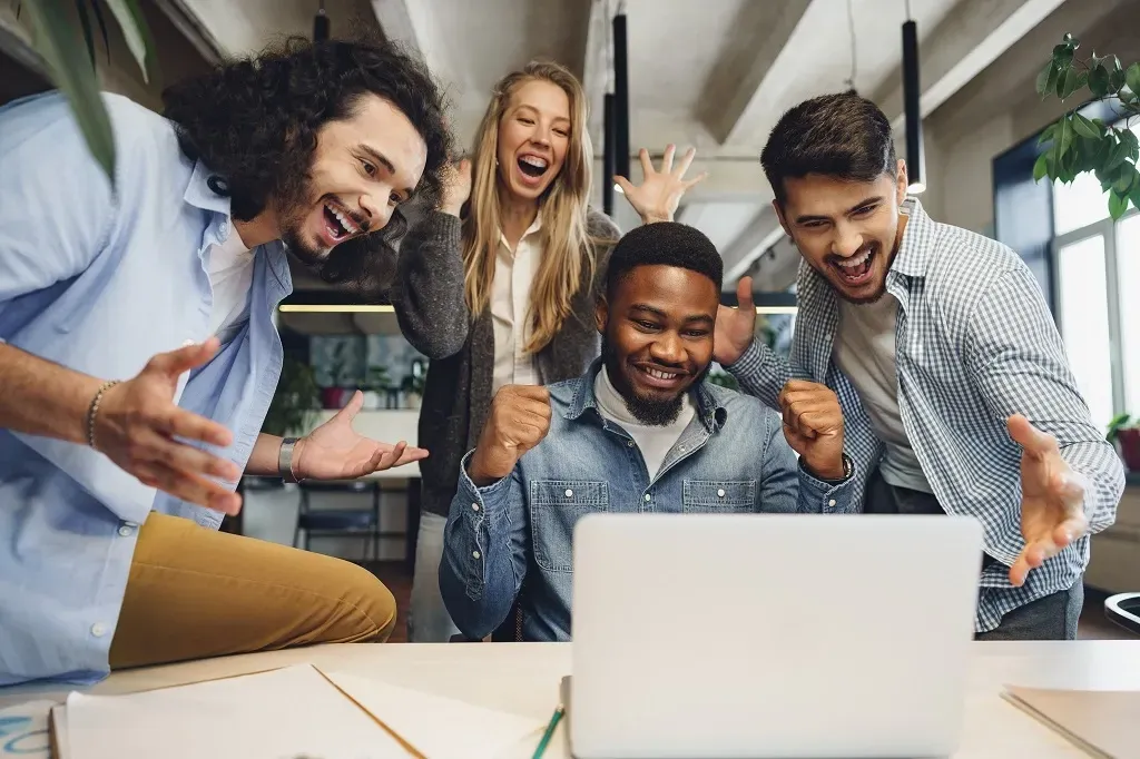 Três homens e uma mulher estão vibrando em frente a um computador