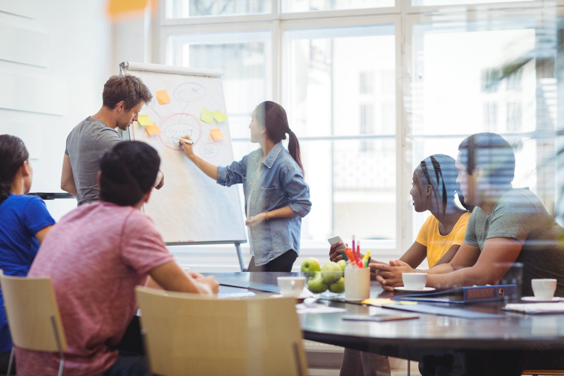 Pessoas em um sala de reunião discutindo, uma escreve no quadro
