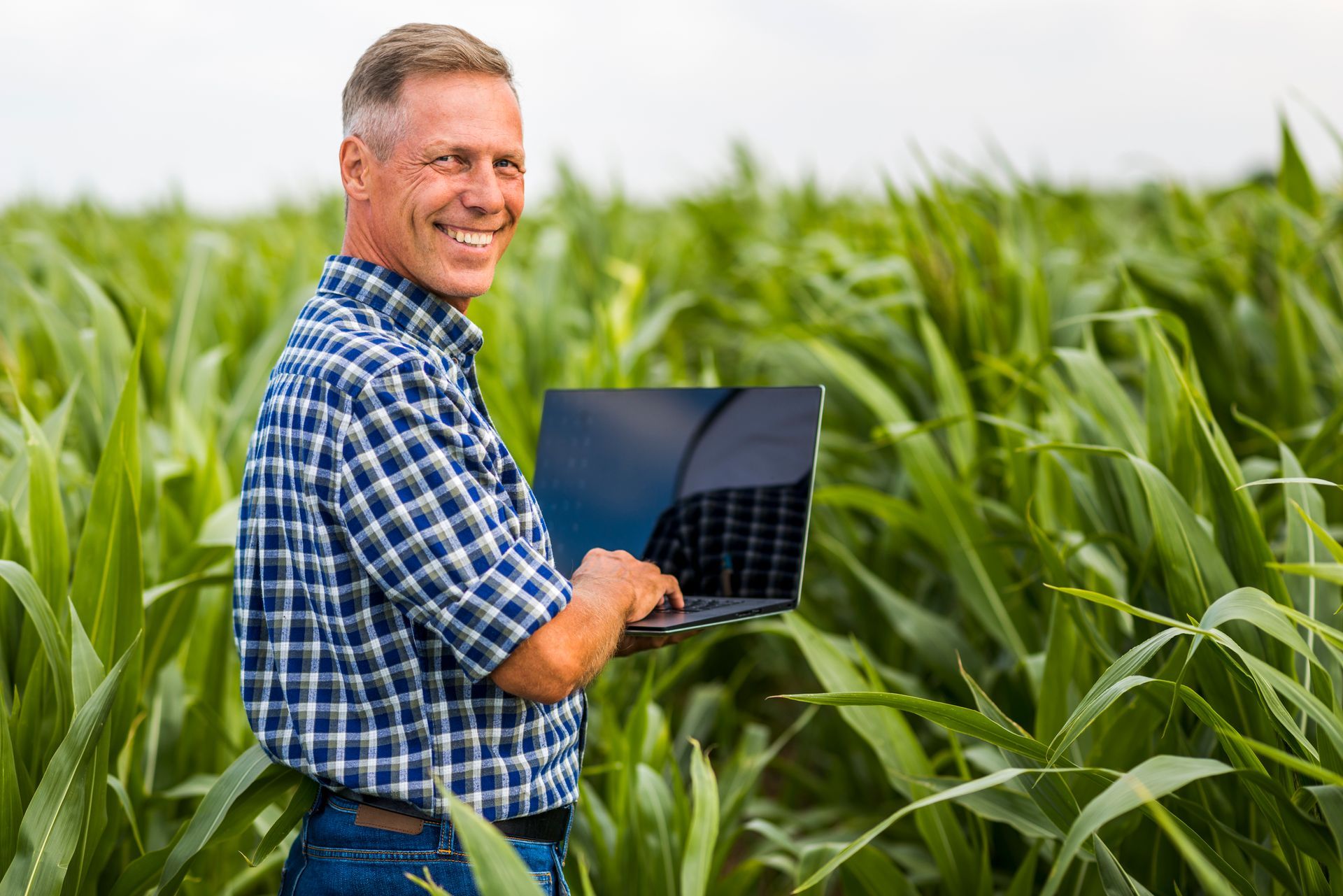 Homem em pé em meio a um campo verde, sorrindo enquanto segura um notebook de gestão de agronegócio.
