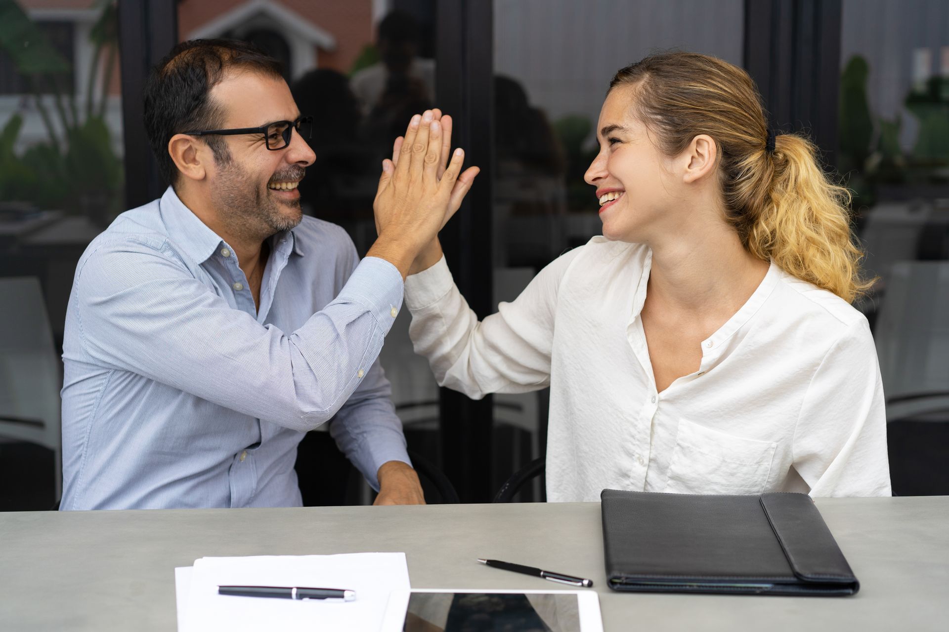 Dois colegas de trabalho batem as mãos sobre a mesa, simbolizando uma liderança humanizada