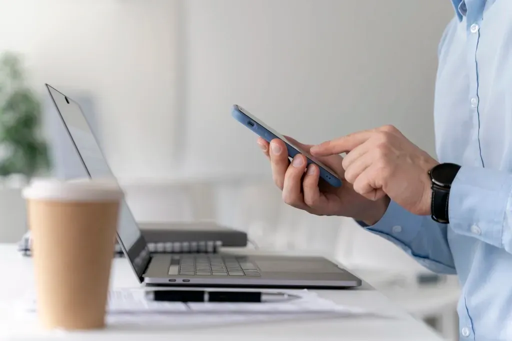 Um homem de negócios jovem trabalhando em sua mesa com lap top e usando o celular