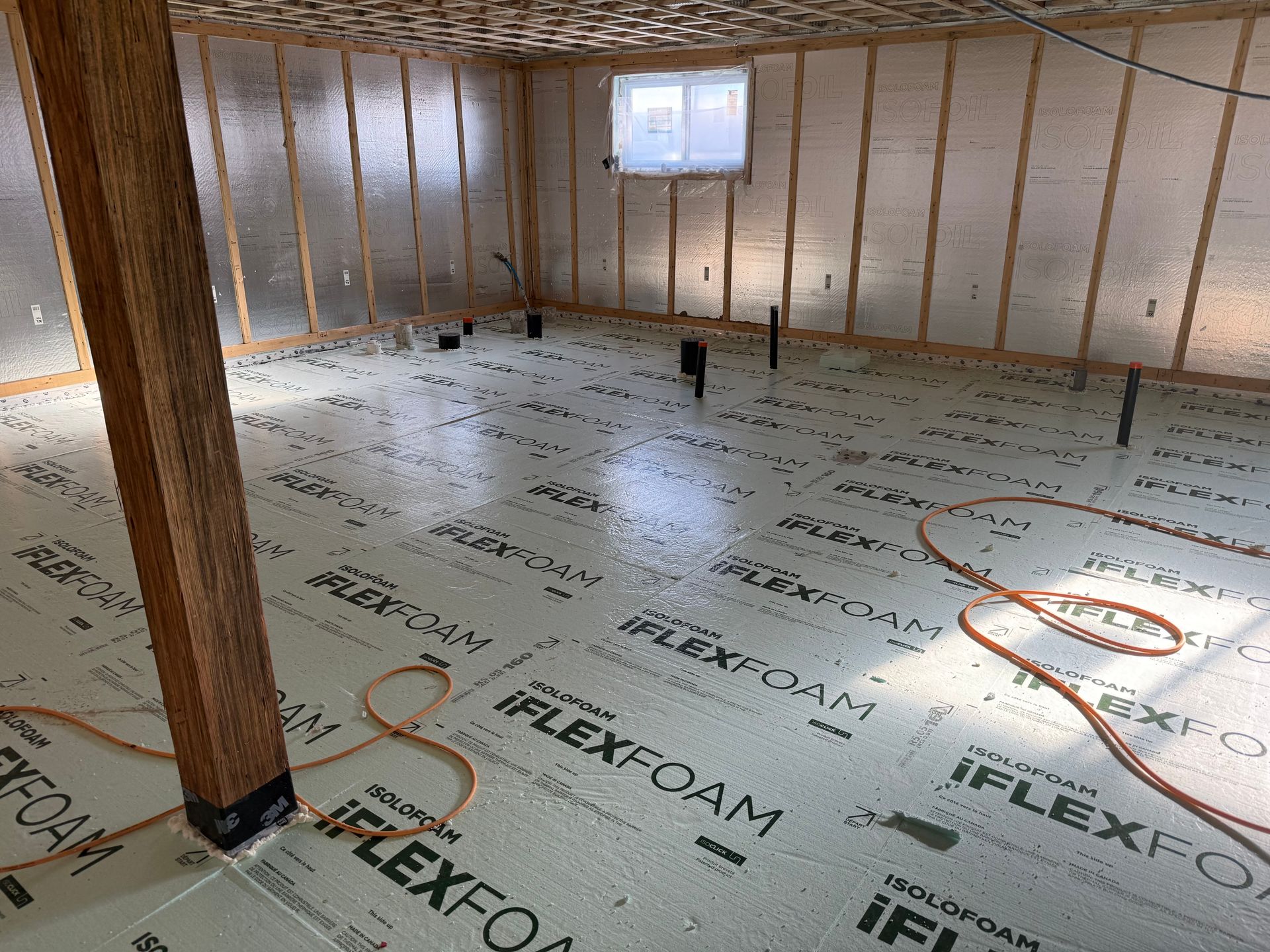 Sous-sol non aménagé avec murs isolés, montants apparents et isolation de plancher réfléchissante posée sur le sous-plancher.