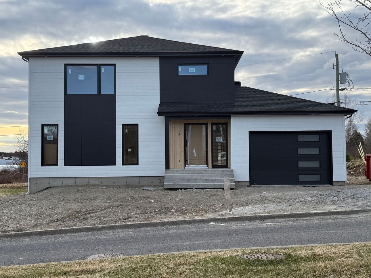 Maison blanche moderne de deux étages avec des accents noirs et un garage pour une seule voiture en bord de route