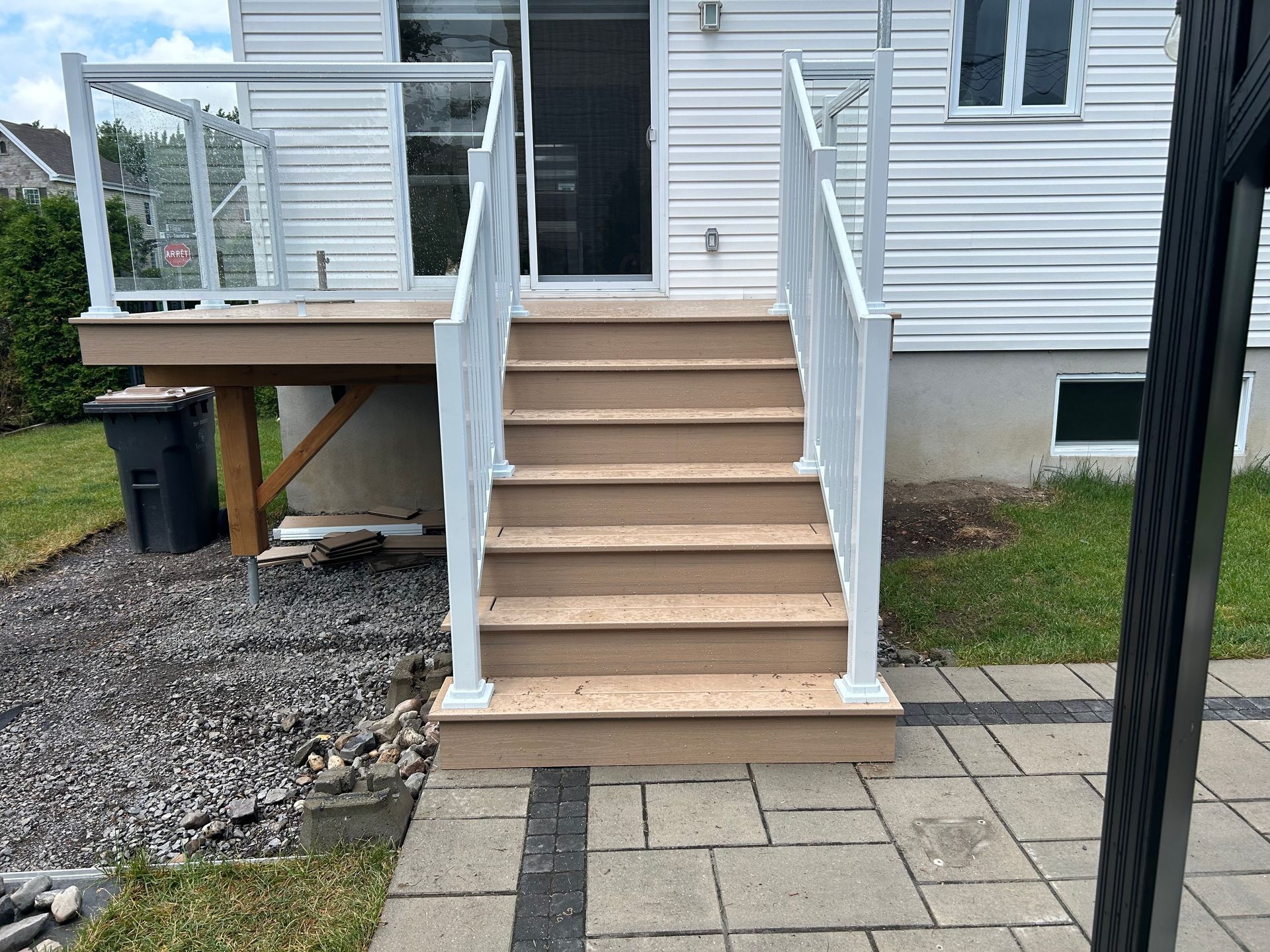 Un escalier avec une rampe blanche mène à l'entrée surélevée de la maison, qui comprend une petite terrasse.