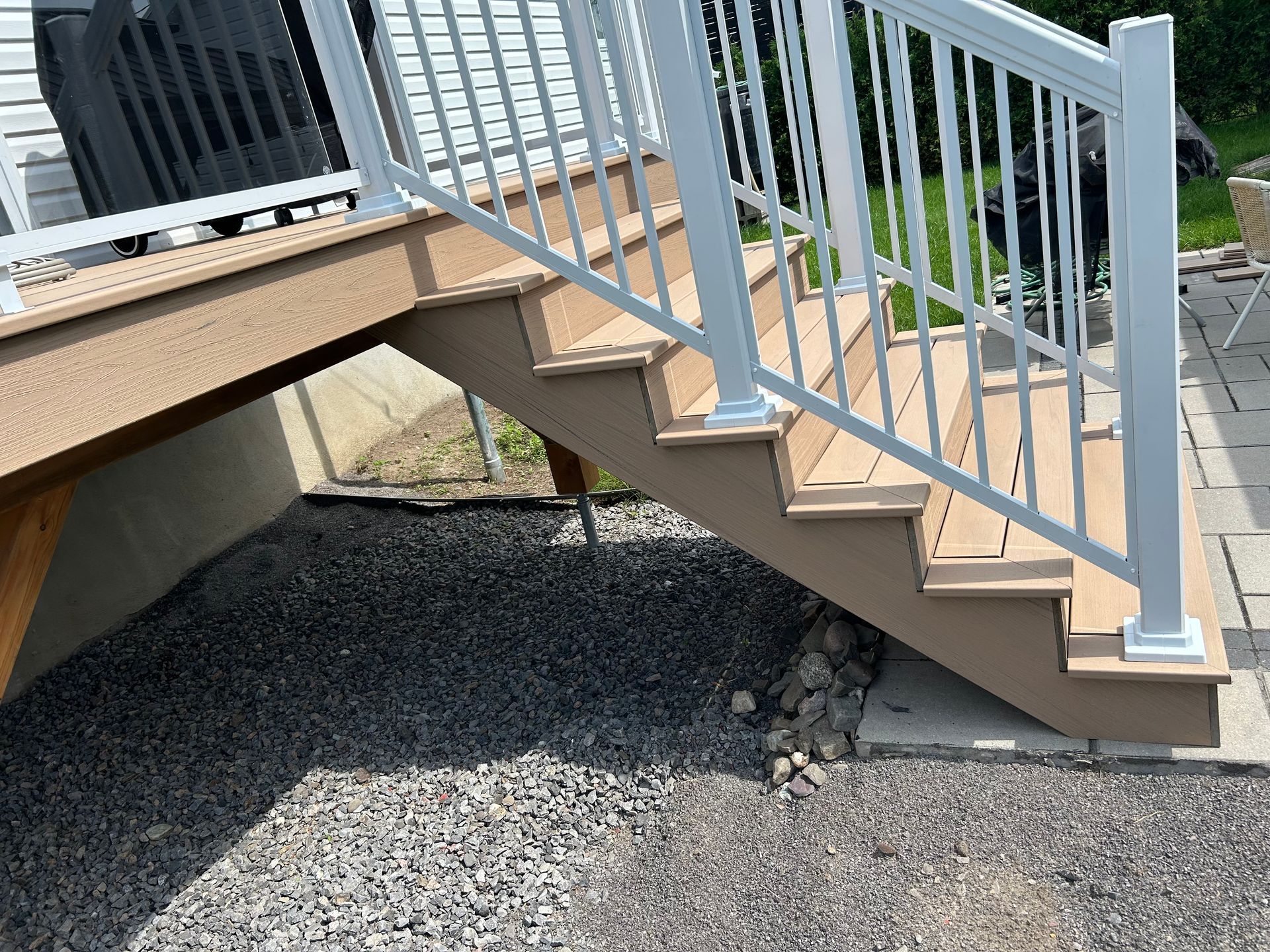 Escalier extérieur en bois avec rampes gris clair donnant sur une zone gravillonnée à côté d'une terrasse