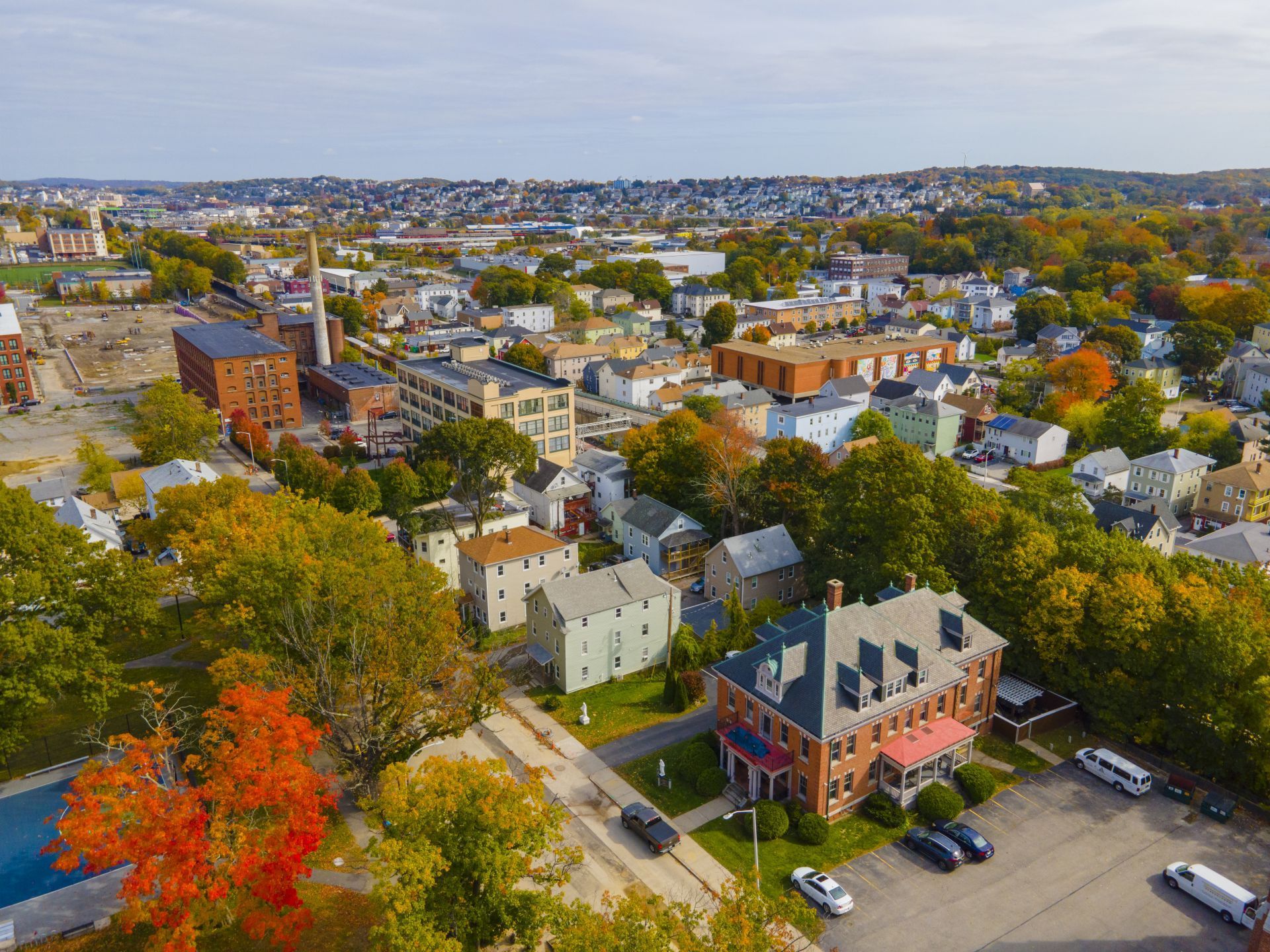 Aerial view of a leafy neighborhood with houses, streets, and autumn-colored trees under a clear sky