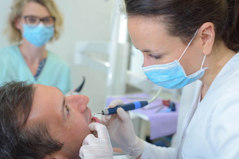 A female dentist is examining a man 's teeth in a dental office.