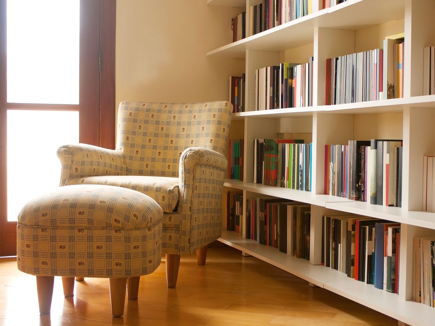 Cozy reading nook with floral armchair, ottoman, and white bookshelves filled with books.