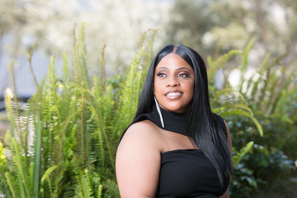 A woman in a black dress is sitting in front of a bush.