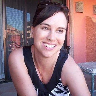 A woman is smiling for the camera while wearing sunglasses and a black tank top.