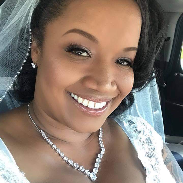 The bride is wearing a veil and a necklace and smiling for the camera.
