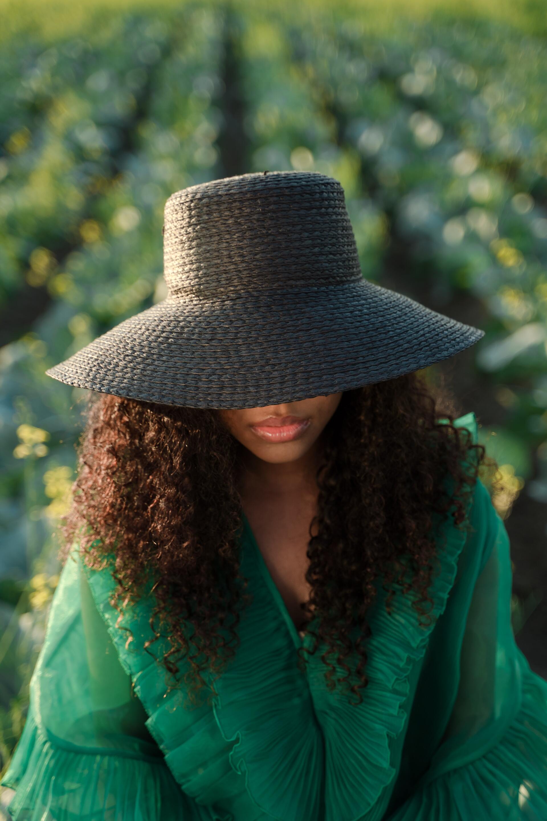 A woman wearing a straw hat and a green dress is sitting in a field of cabbage.