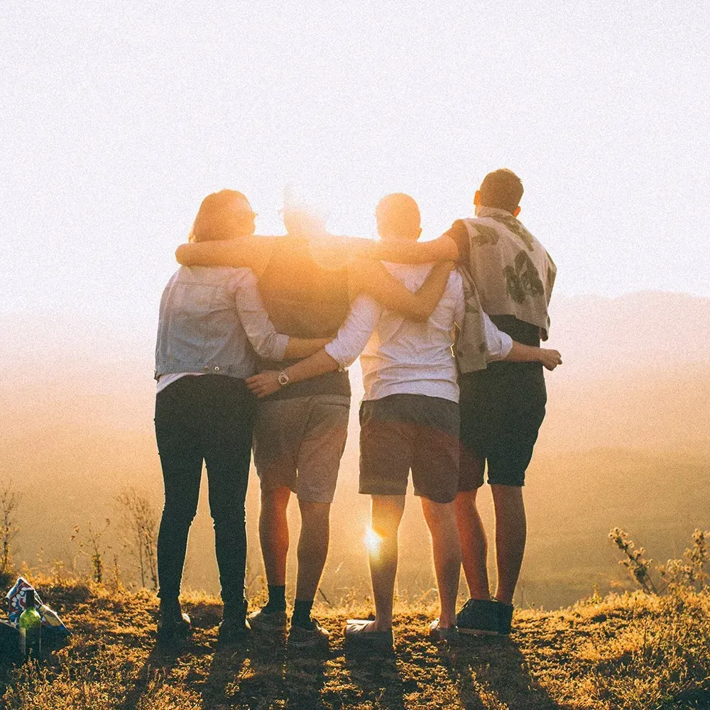 Four people with arms around each other, watching a sunset.
