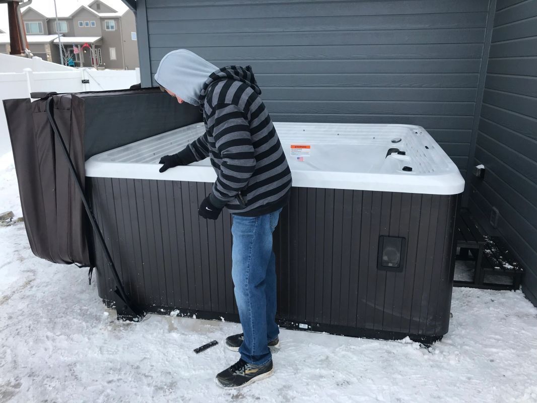 A man is standing next to a hot tub in the snow