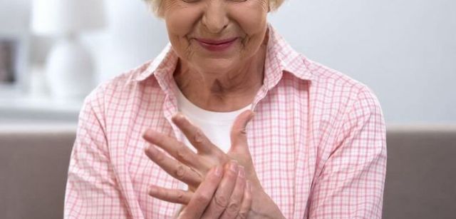 An elderly woman is sitting on a couch holding her hands together.