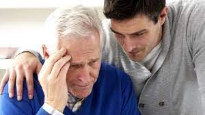 A man is comforting an older man who is having a headache.