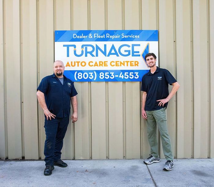 Mechanics in front of a sign for Turnage Auto Care Center | Turnage Auto Care Center