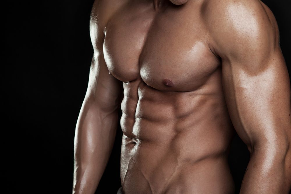 A close-up of a well-defined, muscular torso against a black background — A Bit Cheeky The Adult Store In Lismore, NSW