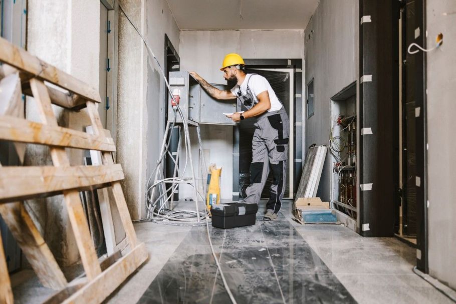 Worker using a drill in a construction hallway with pallets and tools nearby