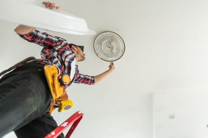 Person on a ladder changing a ceiling light bulb with a wrench