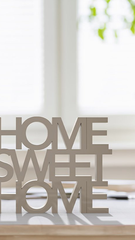 Decorative “HOME SWEET HOME” sign on a bright windowsill with blurred greenery outside