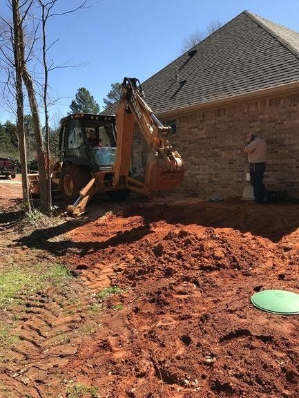 A tractor is digging in the dirt in front of a house.