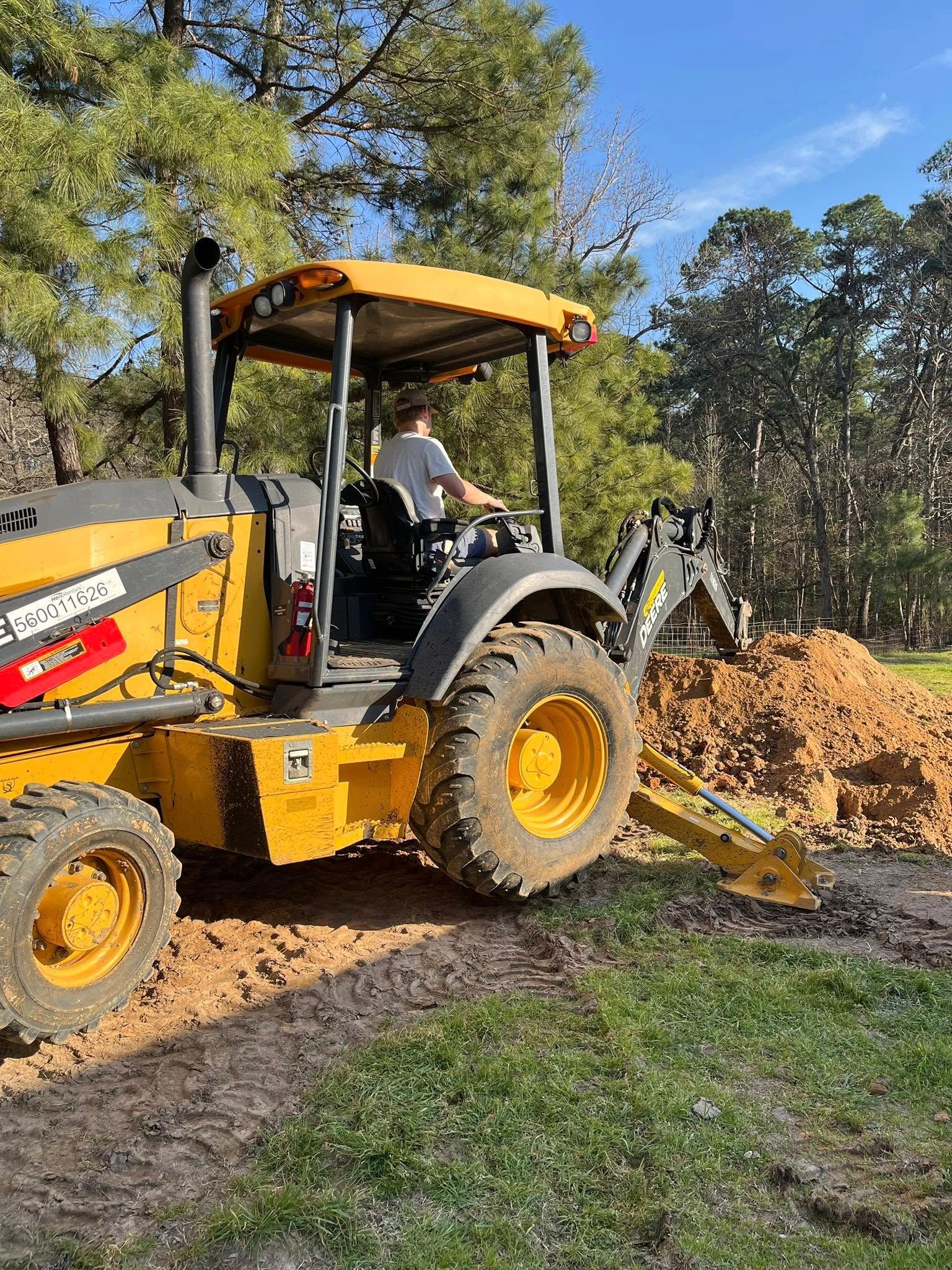 A man is driving a yellow tractor on a dirt road.