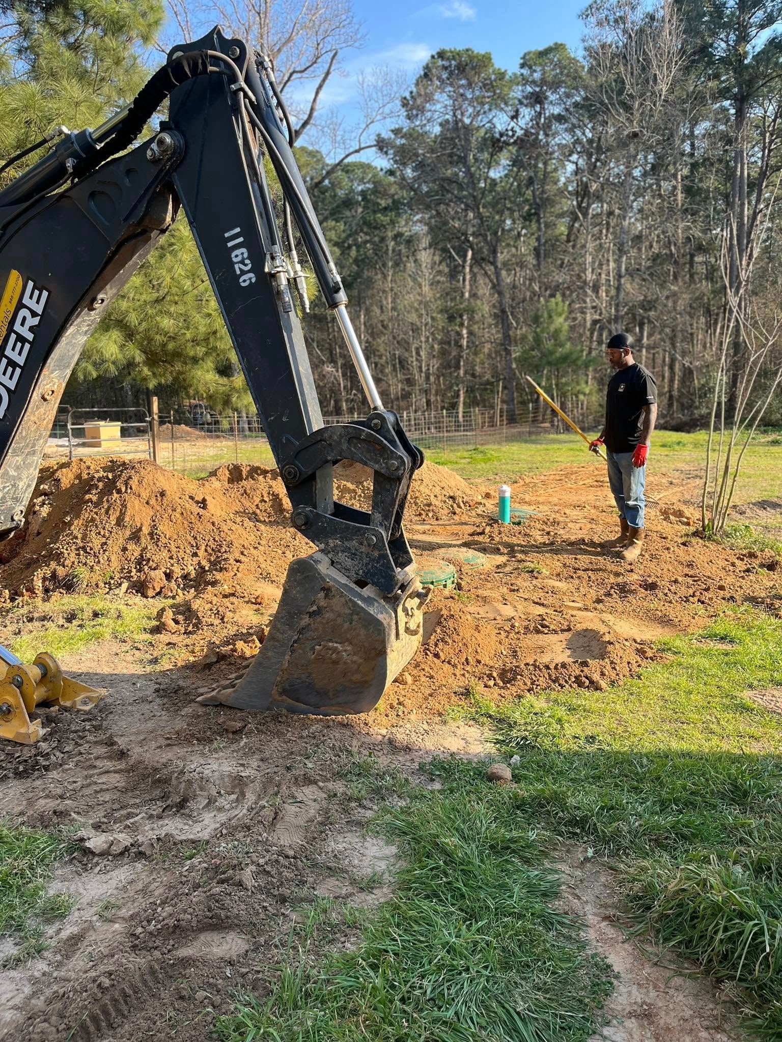 A man is standing next to a large excavator in a dirt field.