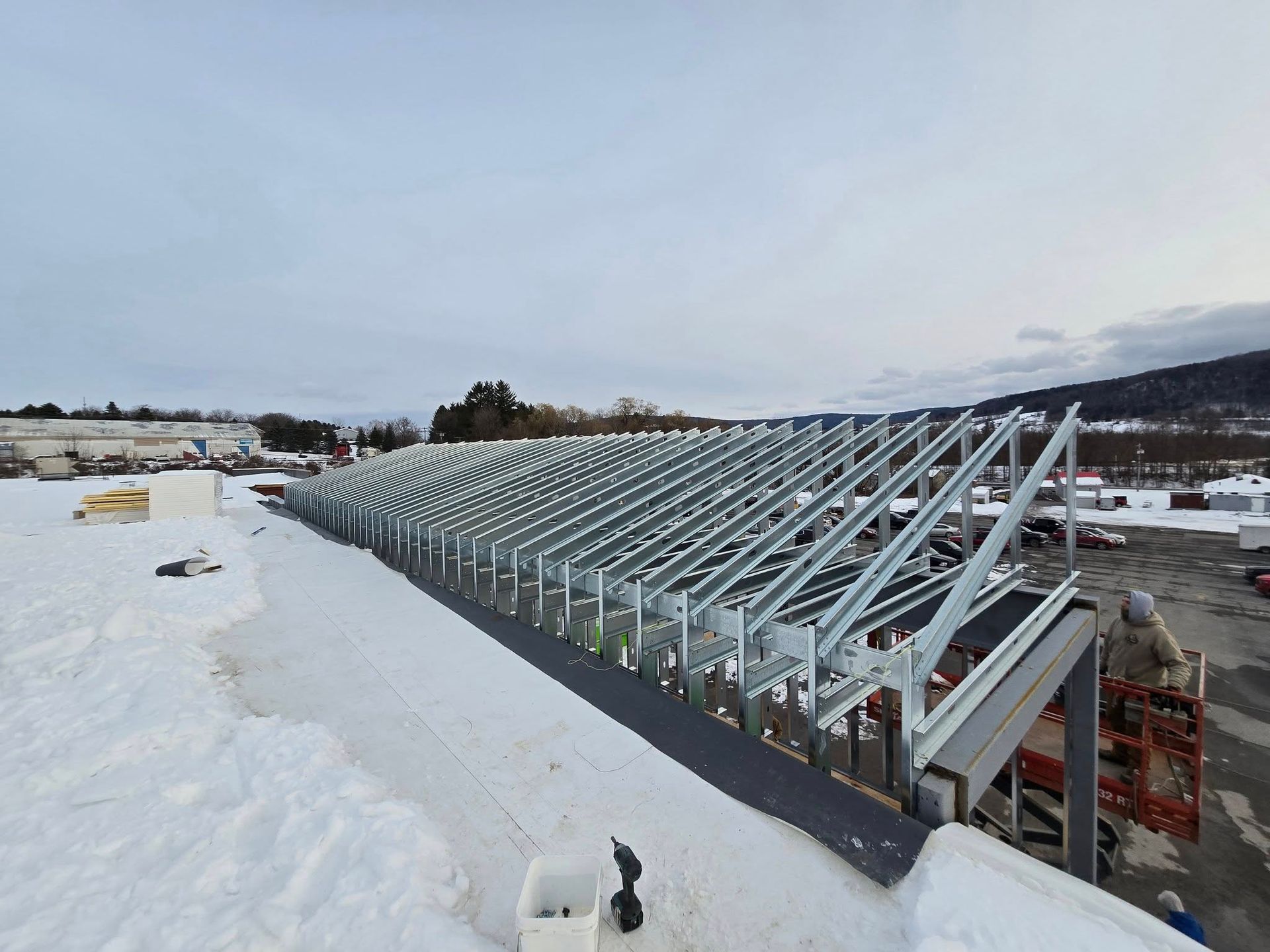 Snow-covered greenhouse frame under construction beside a snowy hillside.