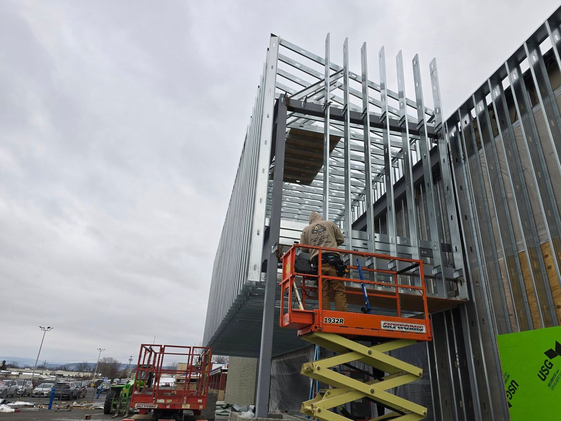 Scissor lift workers installing vertical metal panels on a modern building exterior under cloudy skies