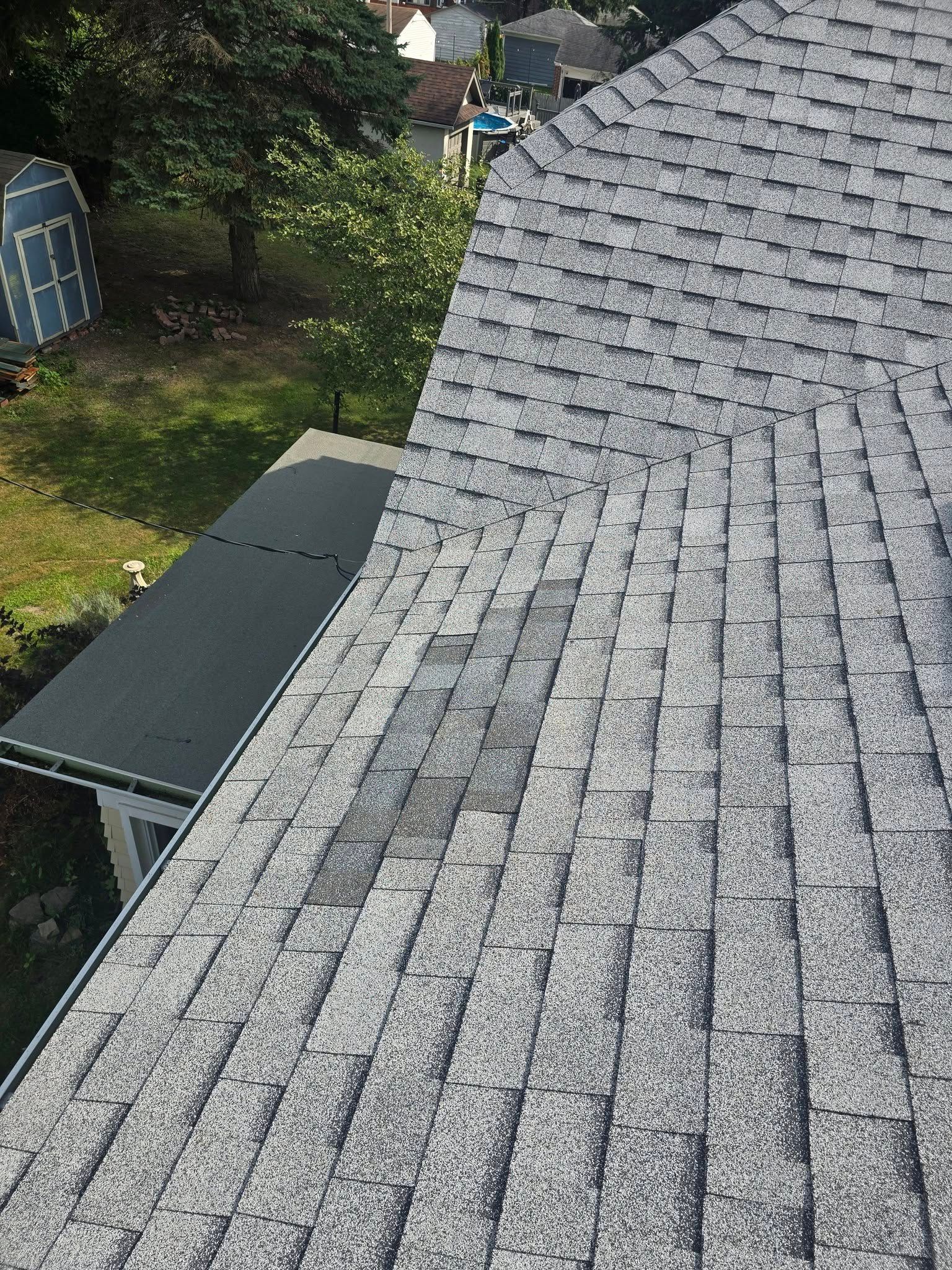 Gray shingled roof beside a small shed and green yard seen from above