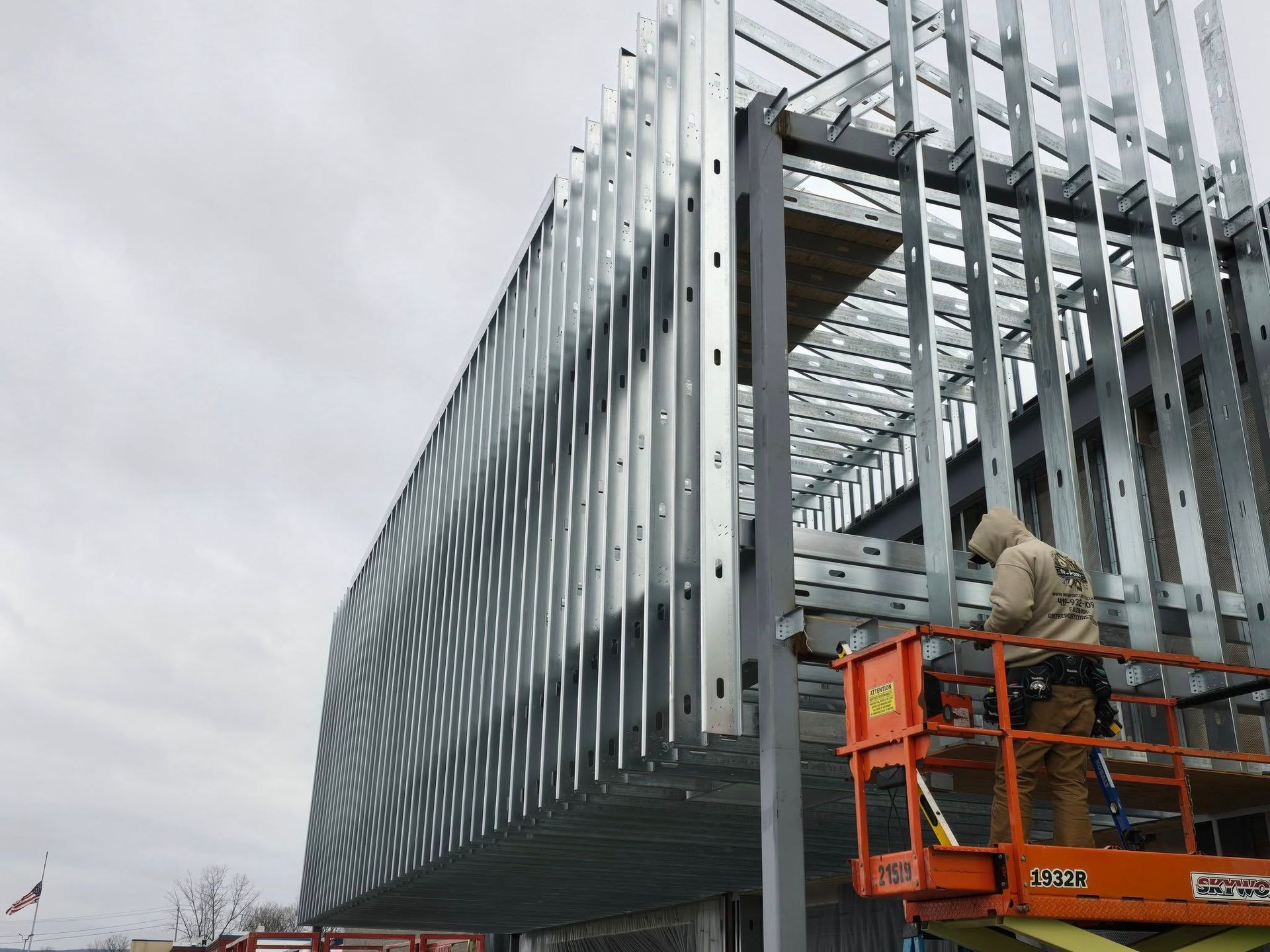 Workers on orange lift installing steel beams on a modern building frame under cloudy sky