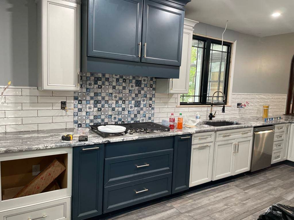 Modern kitchen with navy cabinets, white subway tile, gray countertops, and a window above the sink
