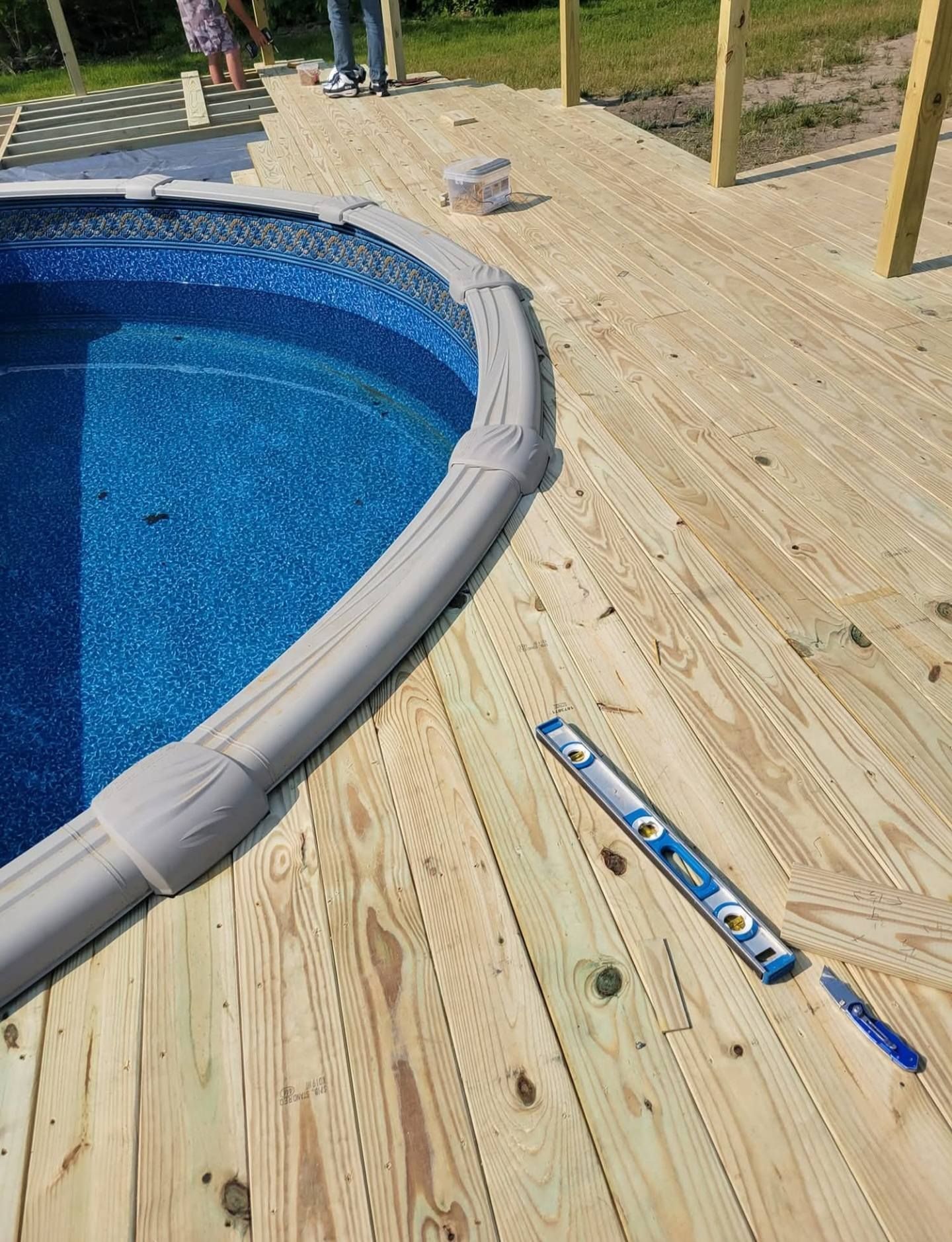 Blue swimming pool beside a wood deck with a level and pen lying on the planks.