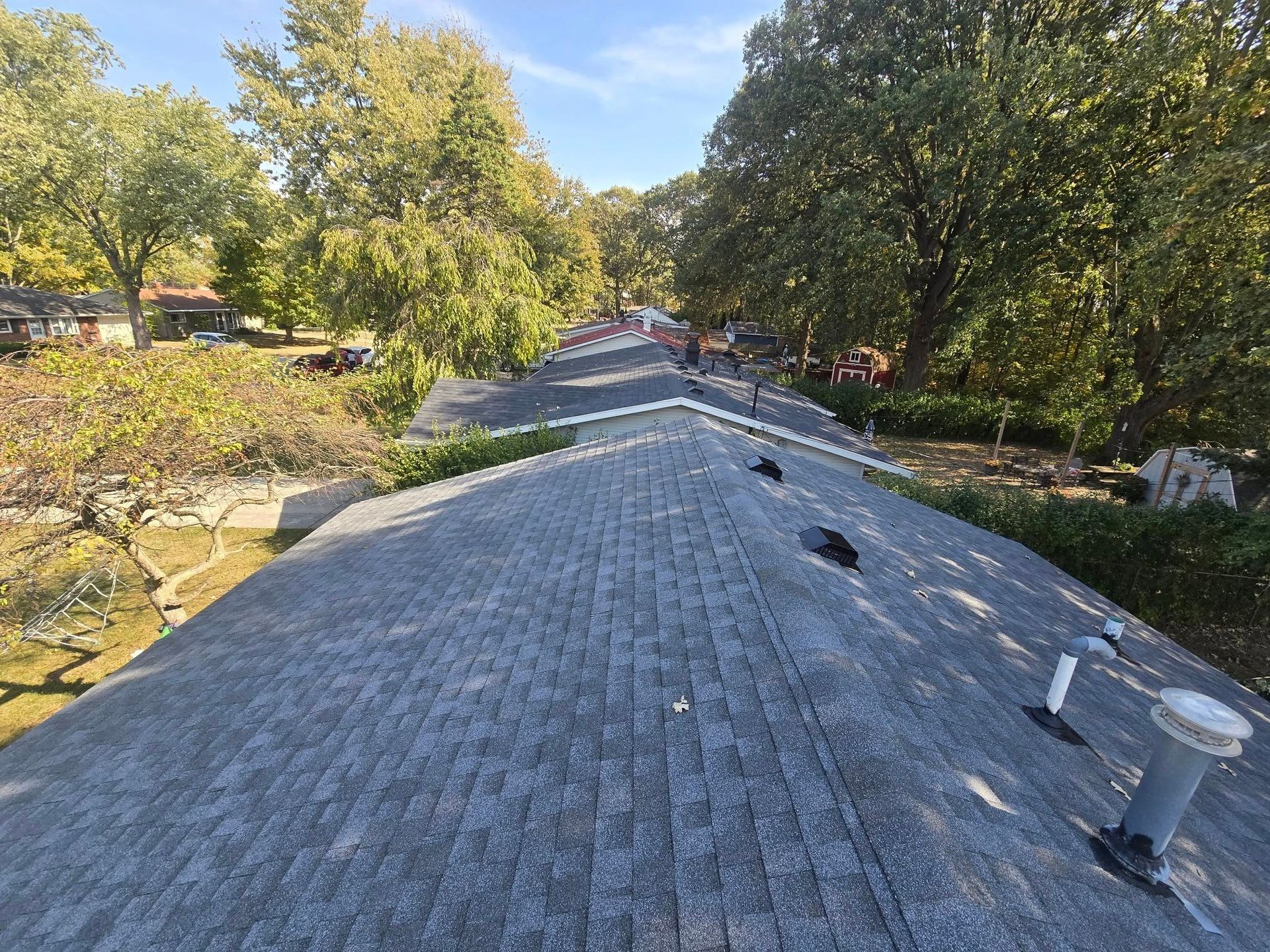 Rooftop covered in gray shingles with trees and a sunny yard in the background