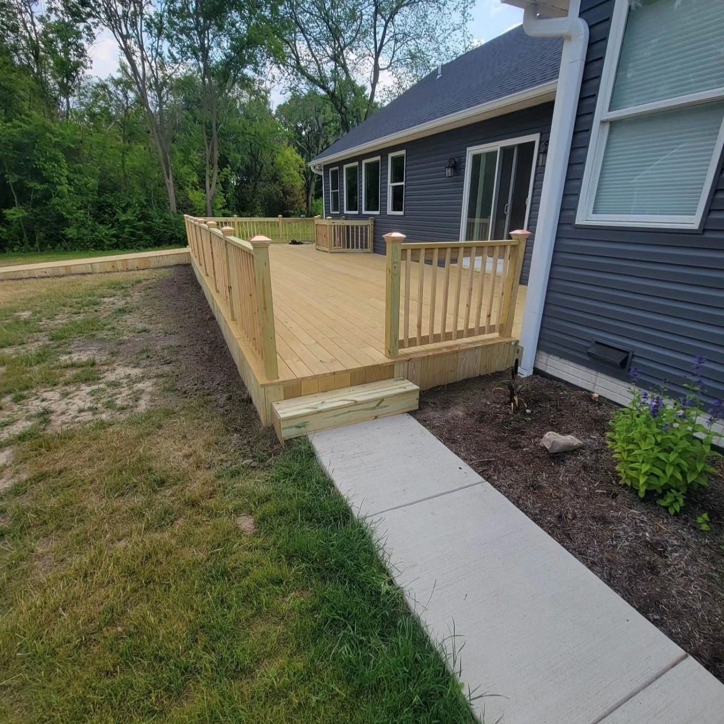 Wooden backyard deck with railings beside a gray house and a concrete walkway