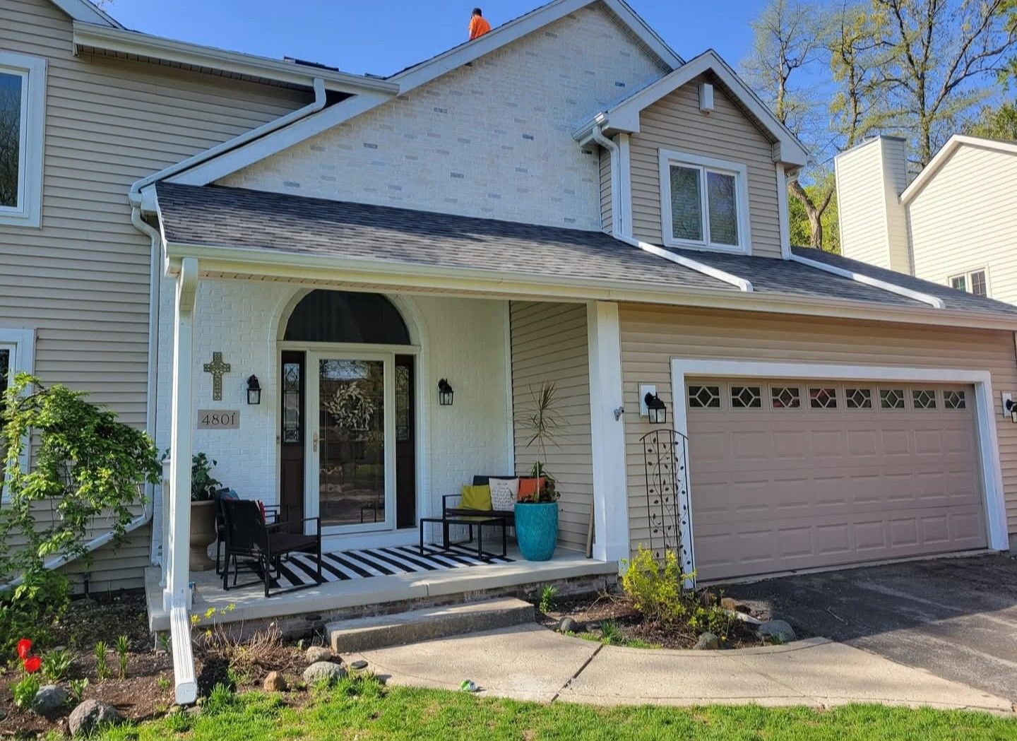 Suburban house exterior with covered front porch, beige siding, and two-car garage door