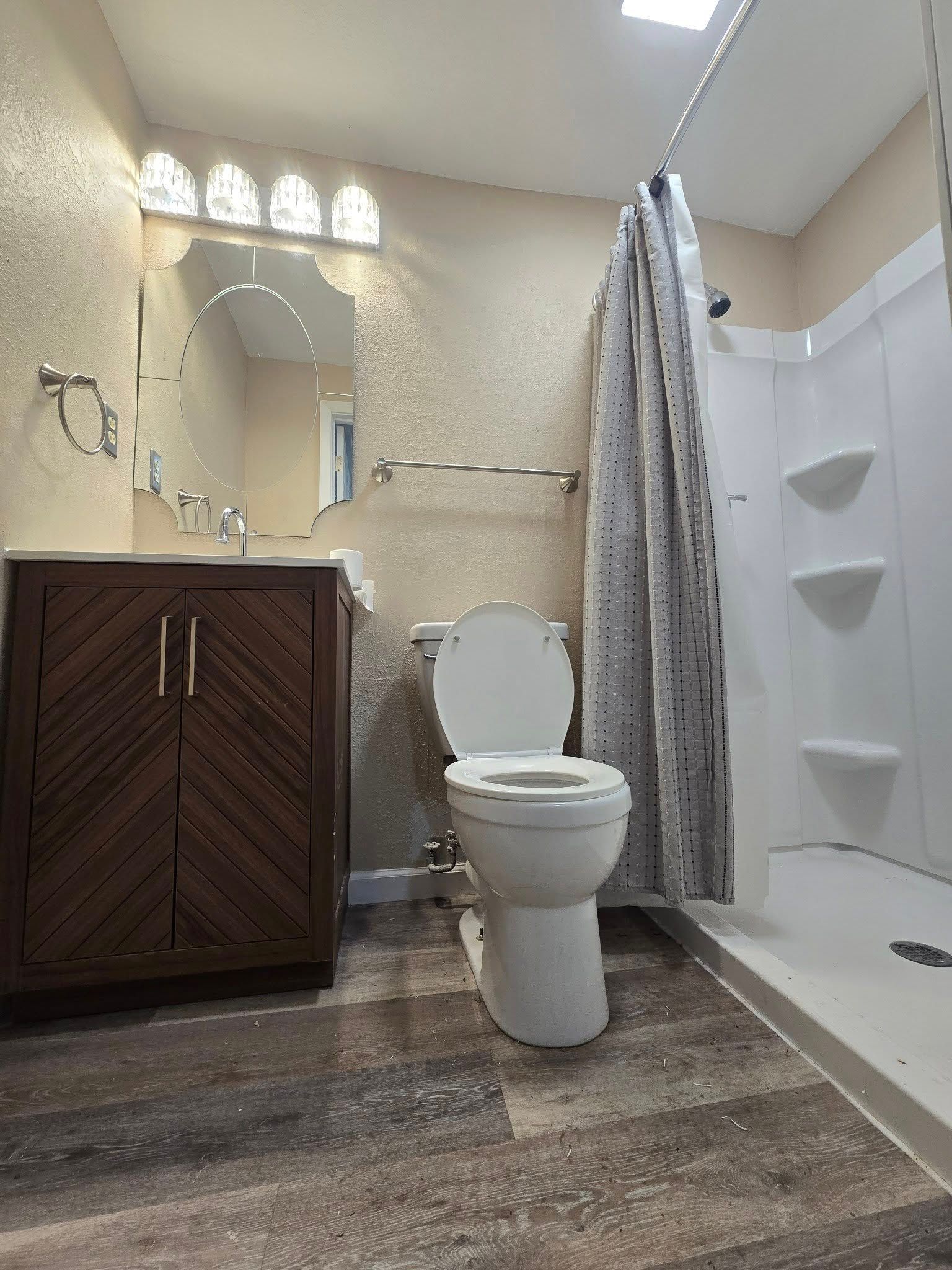 Bathroom with vanity, toilet, and shower stall, featuring beige walls and dark wood flooring.