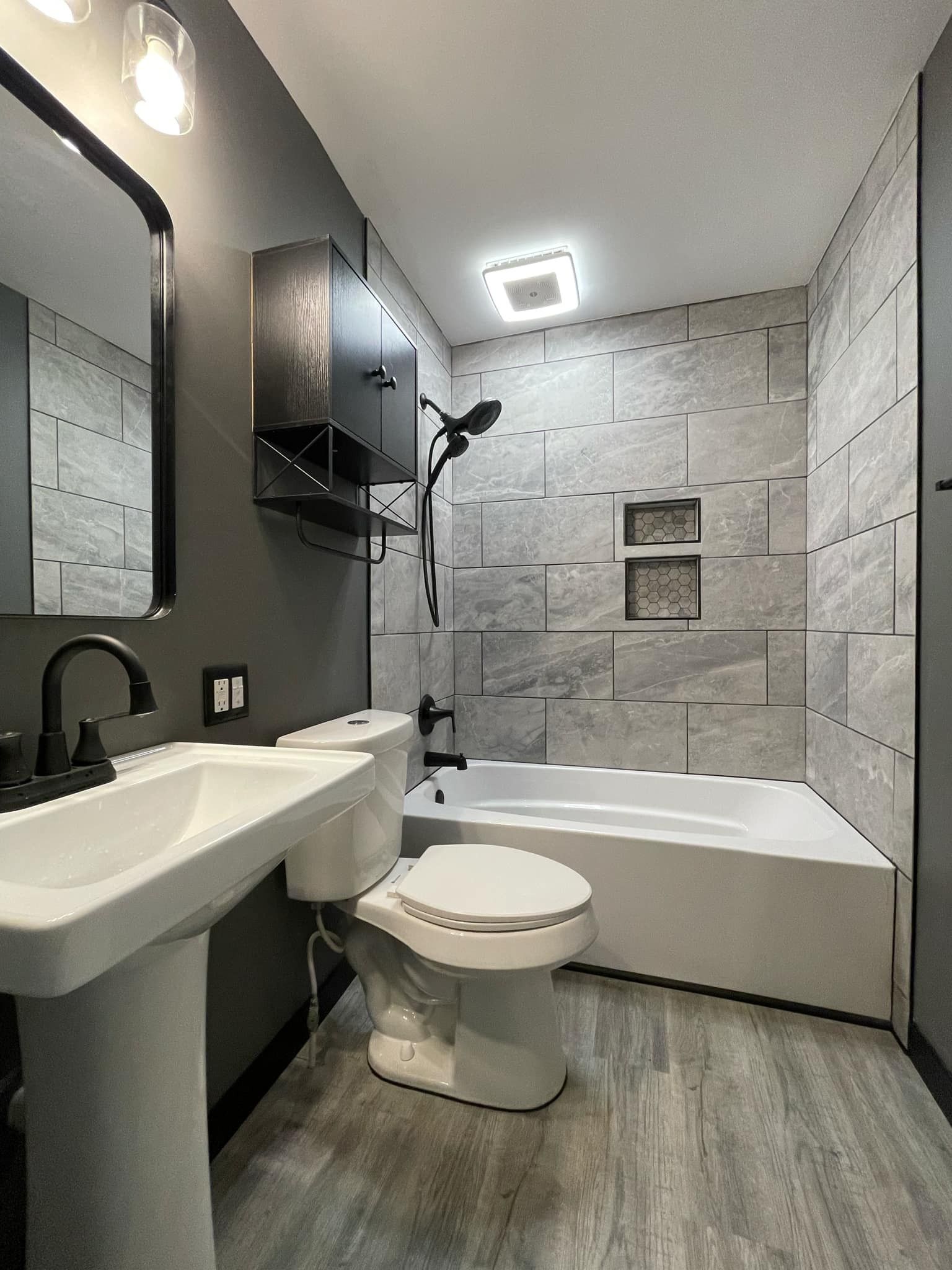 Small modern bathroom with a sink, toilet, bathtub, and gray tile walls and floor.