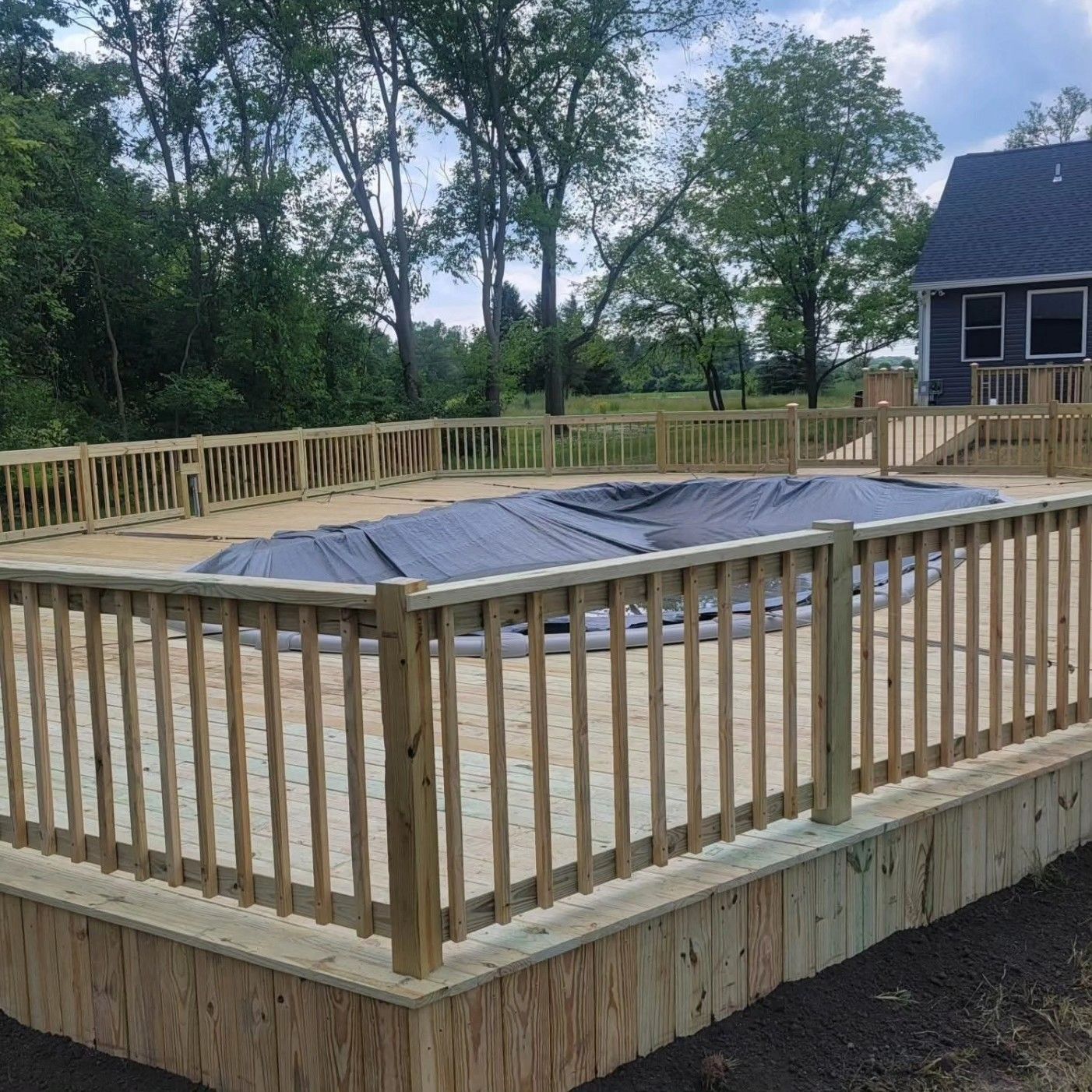 Wooden deck framing under construction beside a white railing, with trees and potted plants nearby