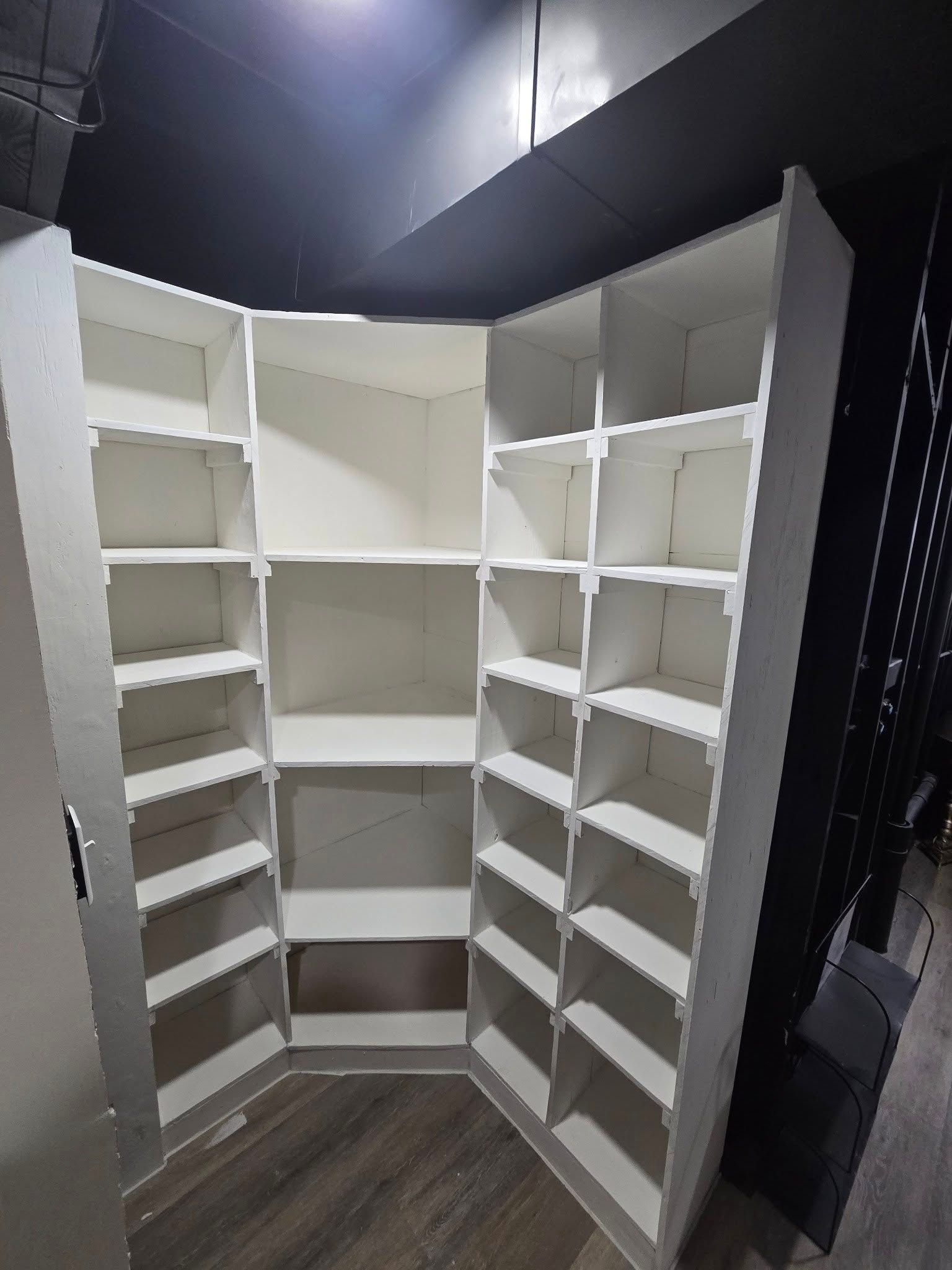 White corner pantry shelves with multiple built-in shelves and dark ceiling trim.