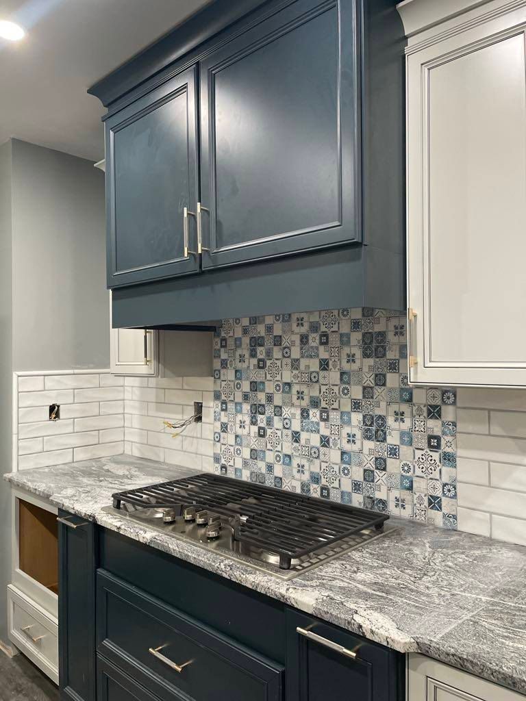 Modern kitchen with blue cabinets, mosaic tile backsplash, stainless range hood, and white countertops
